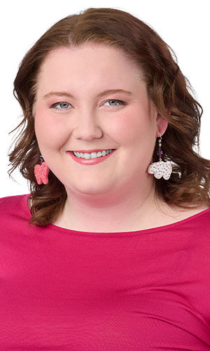Model in a pink shirt wearing design idea S B 2 U pink and white polymer clay animal cracker earrings with colorful sprinkle details, accented by faceted purple crystal beads and finished with silver ear wires.