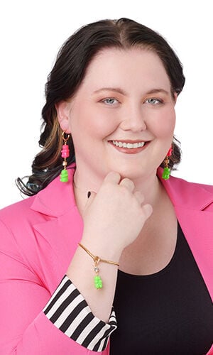 Design Idea S E 2 B - A woman wearing vibrant gummy bear jewelry, including gold dangling earrings with stacked pink and green gummy bears and a matching gold charm bracelet with a green gummy bear charm.