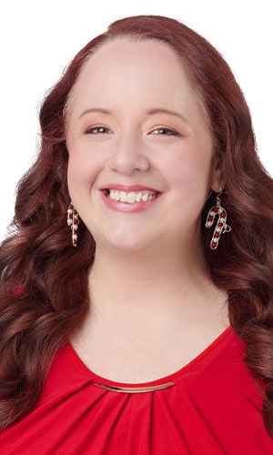 A smiling woman wearing a red top and adorable candy cane dangle earrings accented with small red and white pearls.
