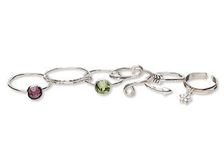 Design Idea M F 3 2 - Six silver rings feature diverse but complementary styles: Two have gemstones, one purple and one green. One has a flower charm. The other two are open spiral rings. One is an arrow that twists around to form a ring. The other has swirls of metal. 