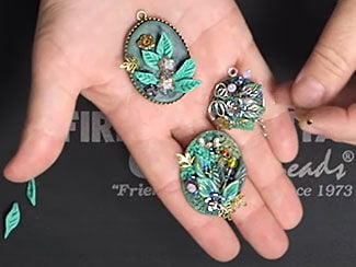 A hand holding three pendants with polymer clay leaf and flower designs on them